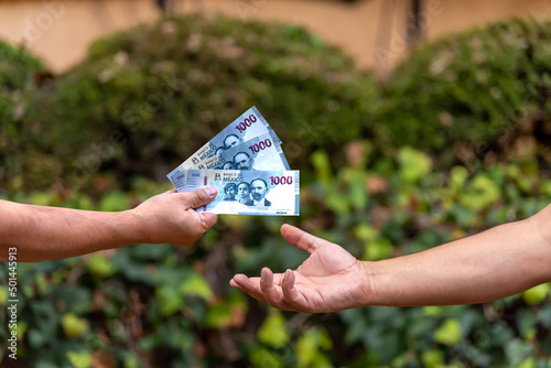 Payment - Hand holding mexican pesos,  new bill designs