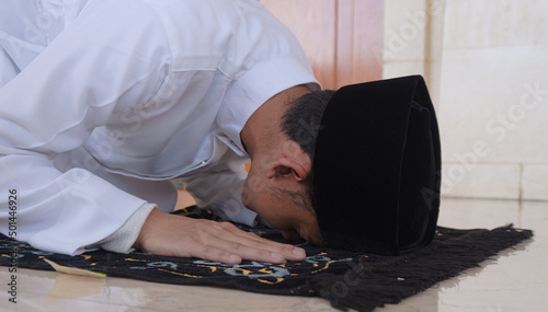Portrait of a Muslim man praying in an act of prostration called Sajdah or prostration. Side view of a Muslim man praying with a prostration pose on the ground in a mosque photo