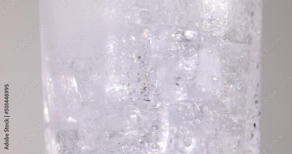 Clear transparent soda water pouring into a tall glass filled with ice fizz bubble foam floating up on white background Clear transparent soda water pouring into a tall glass filled with ice fizz bubble foam floating up on white background