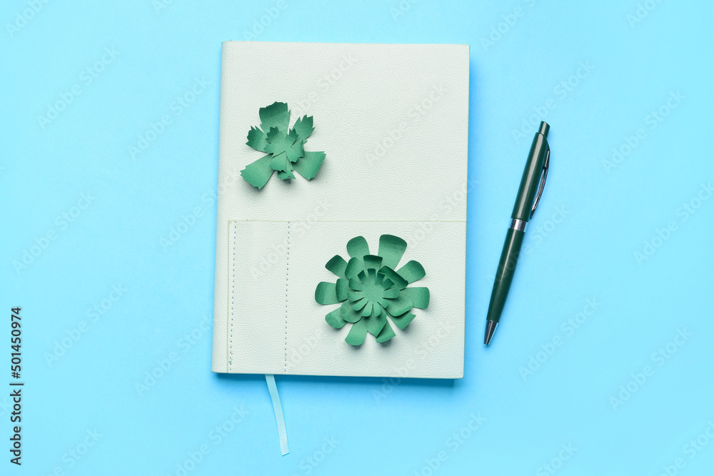 Notebook with pen and paper flowers on color background Notebook with pen and paper flowers on color background