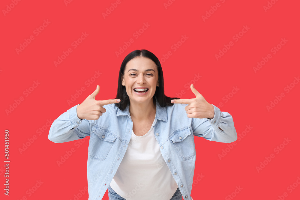 Beautiful woman pointing at dental braces on red background Beautiful woman pointing at dental braces on red background