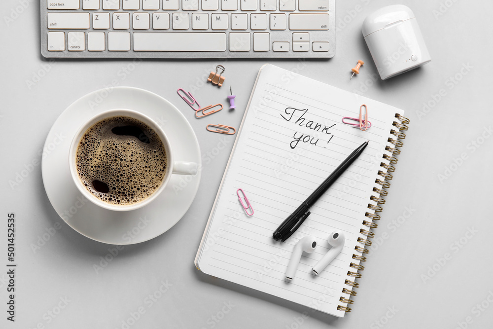 Notebook with text THANK YOU, cup of coffee, earphones and computer keyboard on grey background Notebook with text THANK YOU, cup of coffee, earphones and computer keyboard on grey background