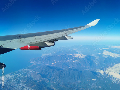 View from the porthole on the wing of an airplane with a red aircraft engine flying to Cyprus in the morning over beautiful mountains with snowy peaks.