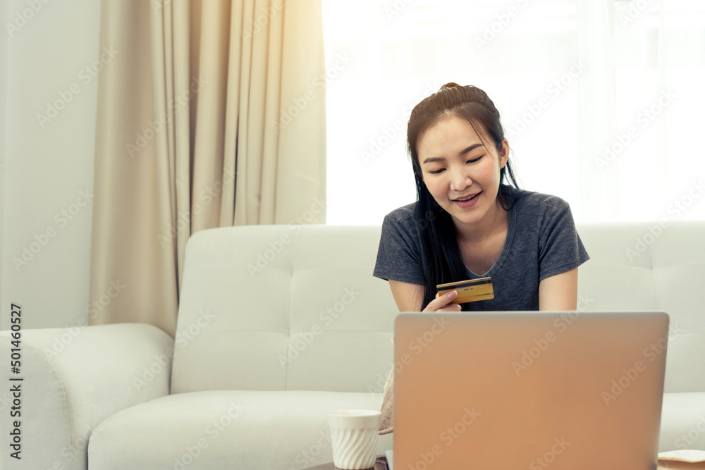 Asian woman holding a credit card for online shopping while sitting on the couch while on vacation at home. Asian woman holding a credit card for online shopping while sitting on the couch while on vacation at home.