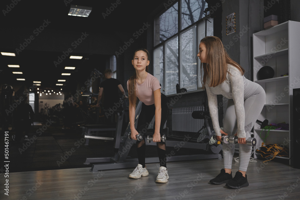 Full length shot of a teen girl and her personal trainer doing dumbbells deadlift exercise at the gym, copy space