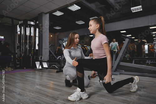 Teen girl doing lunges with weights, working out with personal trainer at the gym