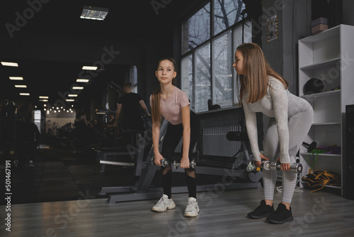 Full length shot of a teen girl and her personal trainer doing dumbbells deadlift exercise at the gym, copy space