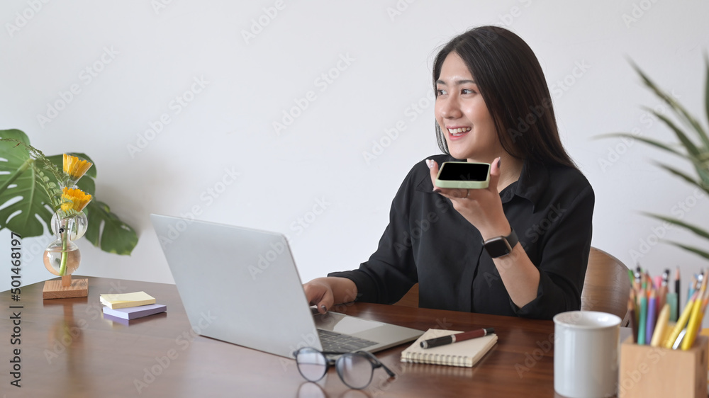 Positive asian woman using laptop computer and having conversation on mobile phone. Positive asian woman using laptop computer and having conversation on mobile phone.