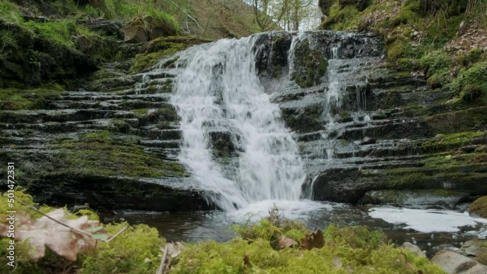 Waterfall in forest 4k slider shot. Showing water running over the rocks with moss and trees in the springtime.