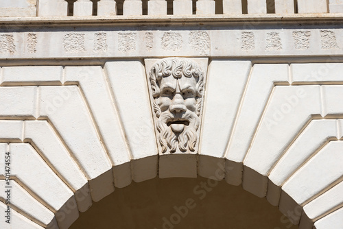 Brescia. Closeup of Medieval Broletto Palace (Palazzo Broletto or Palazzo del Governo), XII-XXI century. White stone arch with keystone and a gargoyle grotesque human mask.  Lombardy, Italy, Europe. photo