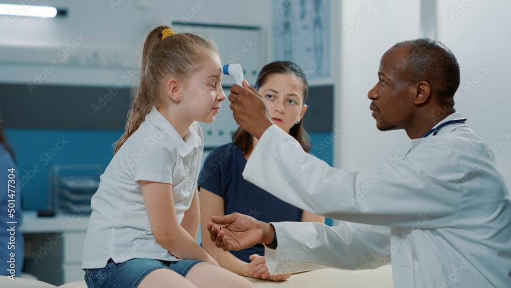 Obraz premium Physician using thermometer on kid to measure temperature in examination cabinet. General practitioner holding medical instrument to check if little child has fever. Health care