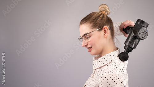 Smiling woman with braces uses a massager gun for her back.