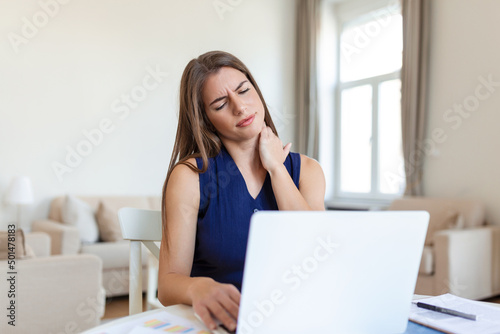 Young Businesswoman Suffering From Neckache. Feeling Tired and Stressed. Frustrated Young Woman Suffering From Neck Pain Massaging her Neck While Sitting at Her Working Place in Home Office