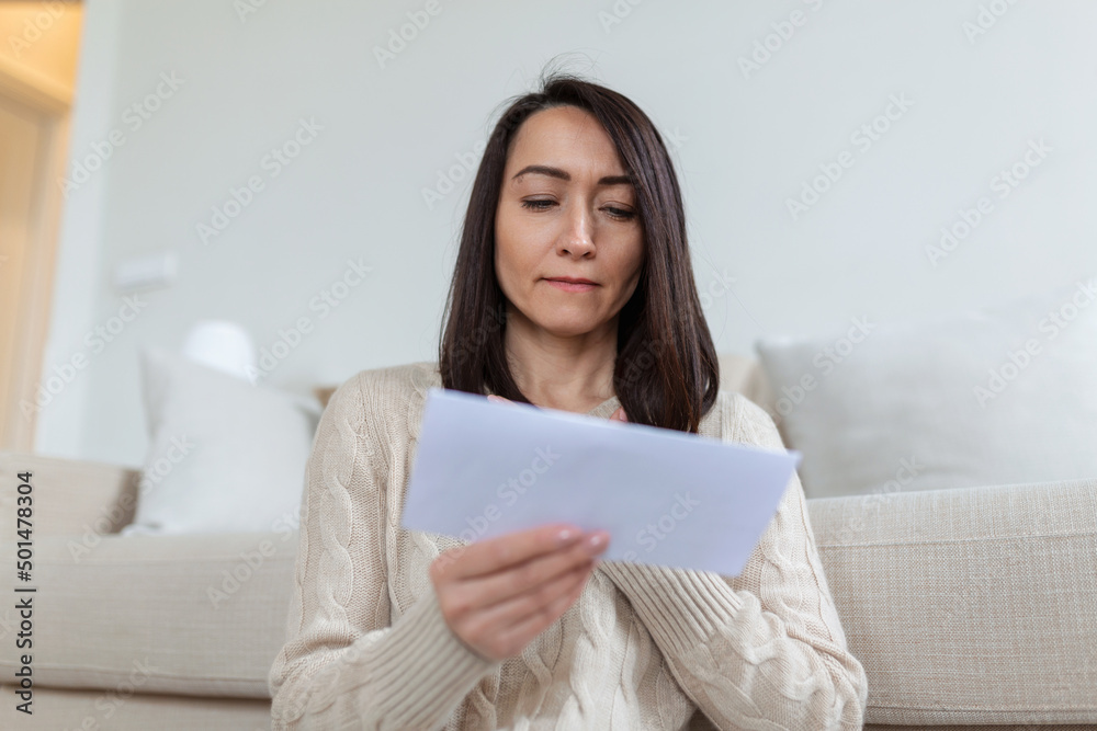 Portrait of a worried Asian woman looking at received letter at home. Beautiful woman with worried facial expression looking at received mail. Portrait of a worried Asian woman looking at received letter at home. Beautiful woman with worried facial expression looking at received mail.