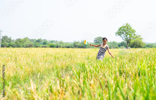 Dancing young village girl kid by holding indian flag at pady agriculture field - concept of freedom, republic or independence celebration and rural India.