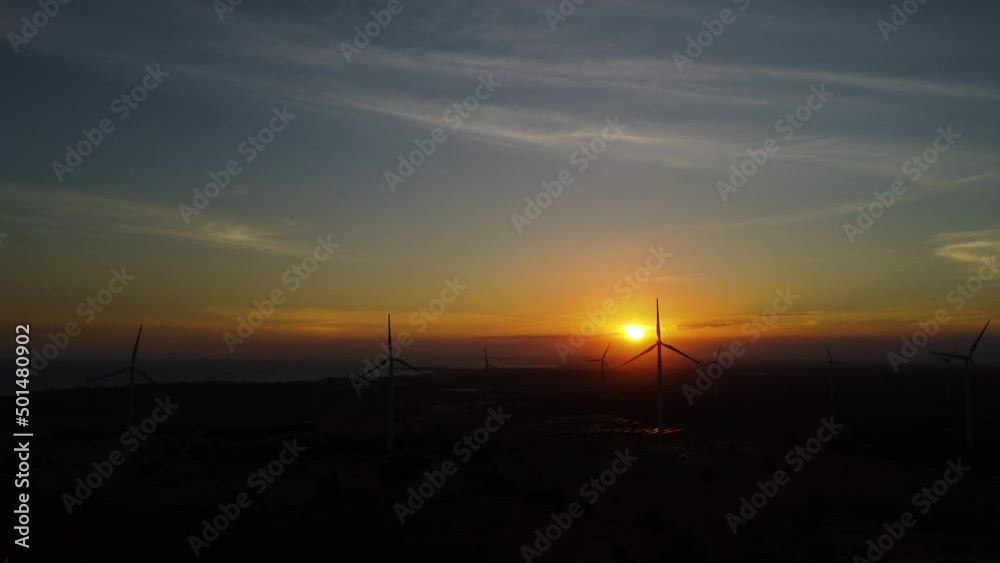 Rotating wind turbines against bright sunset generating energy, aerial view Rotating wind turbines against bright sunset generating energy, aerial view