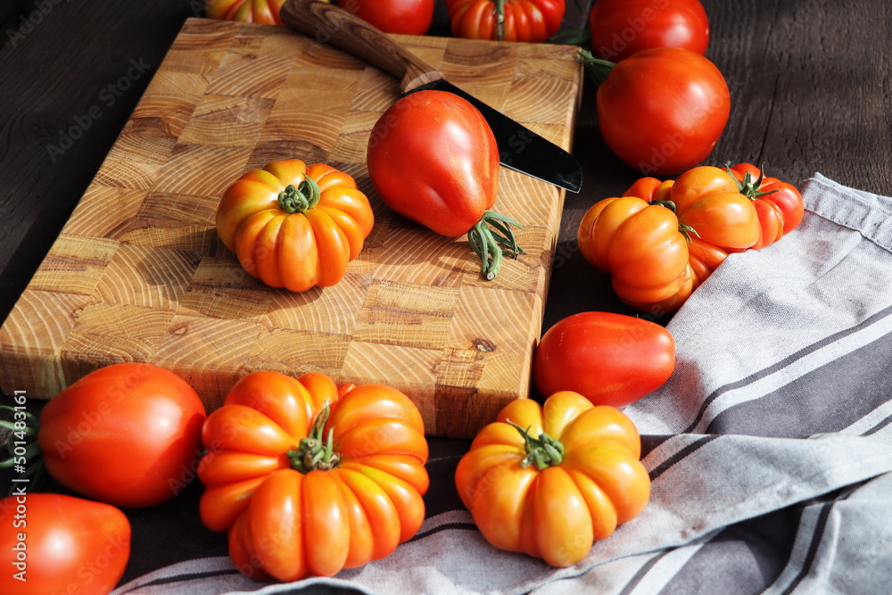 Fresh ripe hairloom tomatoes and knife on rustic wooden board over dark background Fresh ripe hairloom tomatoes and knife on rustic wooden board over dark background