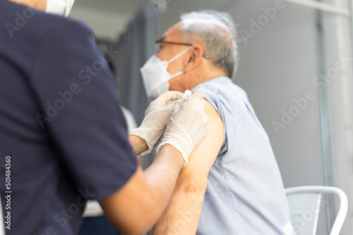 Medical worker perform a vaccine injection to senior Asian man in clinic or medical facility.