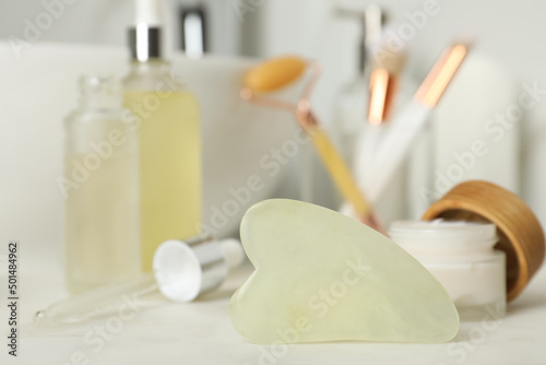 Jade gua sha tool and toiletries on white countertop in bathroom, closeup
