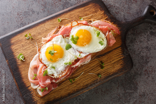 Strammer Max is a German open faced sandwich with ham and eggs closeup on the wooden board on the table. Horizontal top view from above photo