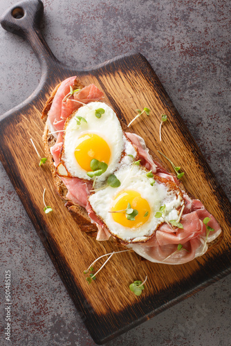 Strammer Max German Sandwich with Cured Ham and Eggs closeup on the wooden board on the table. Vertical top view from above photo