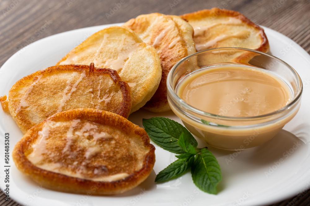 Pile of freshly fried thick pancakes, in Eastern European cuisines called oladky or oladyi with condensed milk on wooden background Pile of freshly fried thick pancakes, in Eastern European cuisines called oladky or oladyi with condensed milk on wooden background
