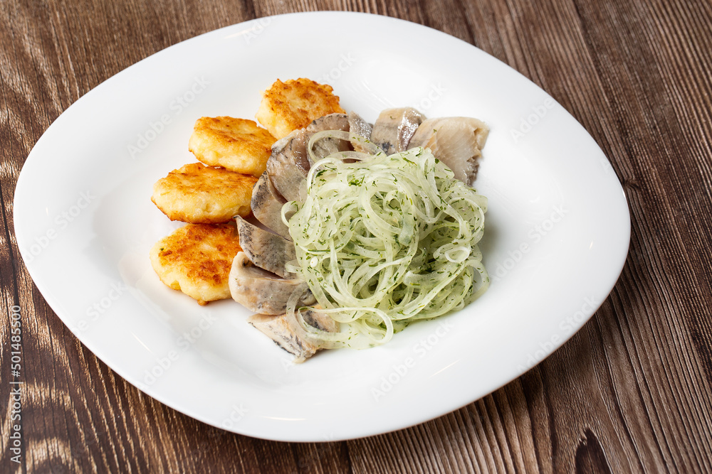 Herring with potatoes and onions on a plate. Ukrainian traditional cuisine on wooden background. Herring with potatoes and onions on a plate. Ukrainian traditional cuisine on wooden background.