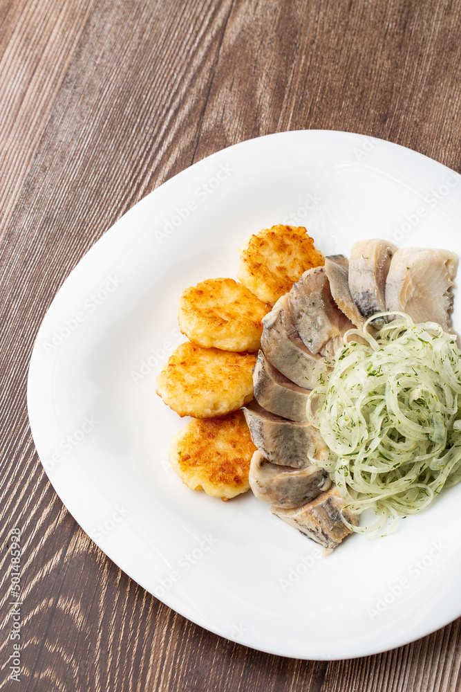 Herring with potatoes and onions on a plate. Ukrainian traditional cuisine on wooden background. Herring with potatoes and onions on a plate. Ukrainian traditional cuisine on wooden background.