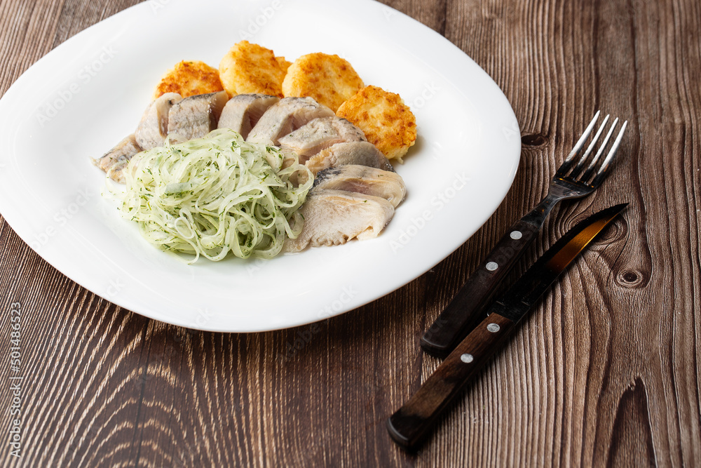 Herring with potatoes and onions on a plate. Ukrainian traditional cuisine on wooden background. Herring with potatoes and onions on a plate. Ukrainian traditional cuisine on wooden background.