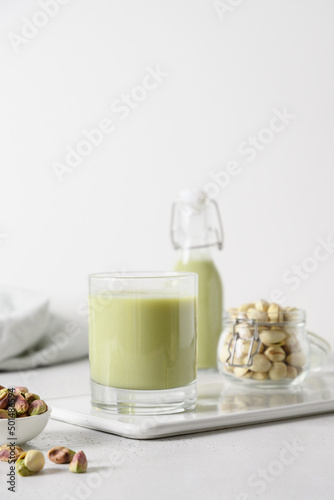 Pistachio milk in glass and pistachios in glass jar on white background. Lactose free. Vegan nutty plant based milk. Vertical.