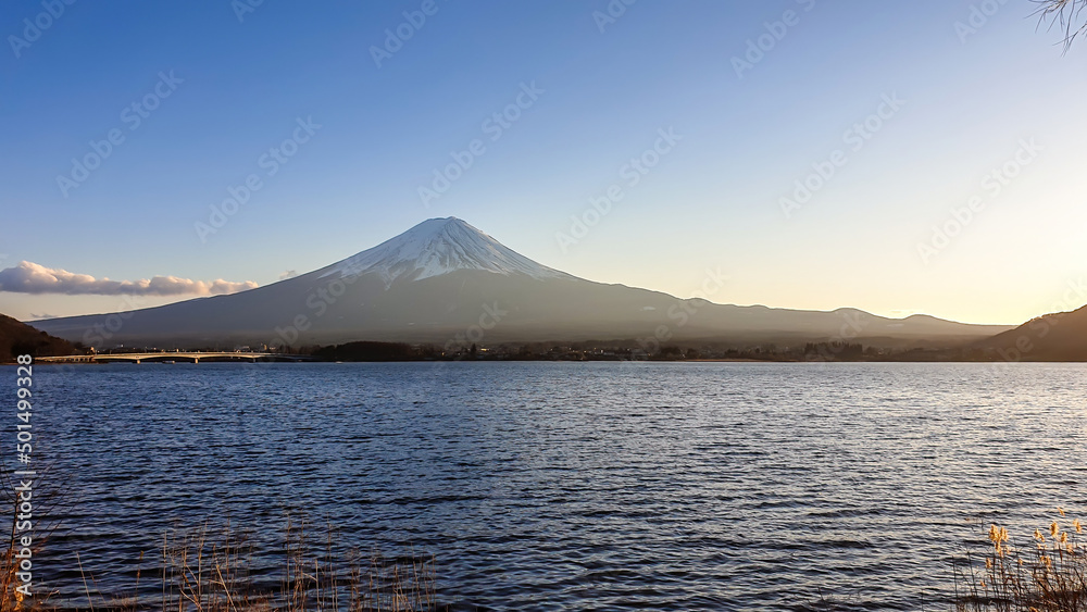Idyllic view on Mt Fuji from the side of Kawaguchiko Lake, Japan. The mountain is surrounded by clouds. Calm surface of the lake moved by gentle wind. Serenity and calmness. Soft colors of the sunset