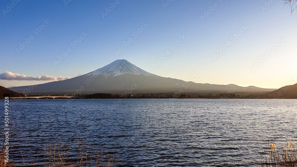 Idyllic view on Mt Fuji from the side of Kawaguchiko Lake, Japan. The mountain is surrounded by clouds. Calm surface of the lake moved by gentle wind. Serenity and calmness. Soft colors of the sunset Idyllic view on Mt Fuji from the side of Kawaguchiko Lake, Japan. The mountain is surrounded by clouds. Calm surface of the lake moved by gentle wind. Serenity and calmness. Soft colors of the sunset