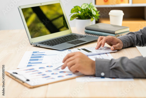businessman or accountant hand working on calculator to calculate business data, accounting document and laptop computer at office, business concept