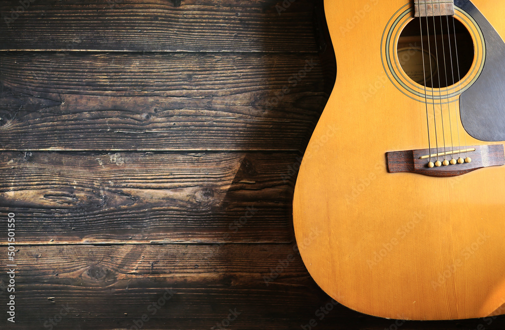 Obraz premium Acoustic guitar on wooden floor, soft light and shadow.