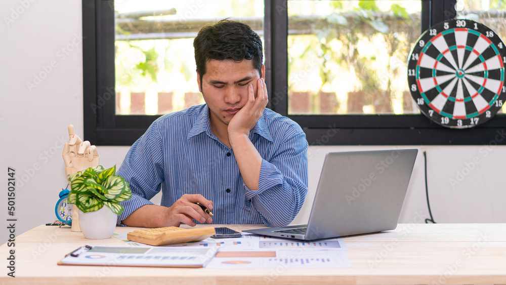 Young Asian businessman working using laptop calculator for accounting planning. Financial graphs and reporting statistics investment and income profits Businessman who analyzes expenses Young Asian businessman working using laptop calculator for accounting planning. Financial graphs and reporting statistics investment and income profits Businessman who analyzes expenses