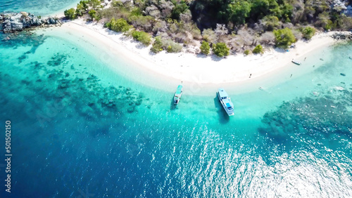 A drone shot of a paradise island with some boats anchored around in Komodo National Park  Flores  Indonesia. Green middle part of the island turns into white sand beach and further into turquoise sea