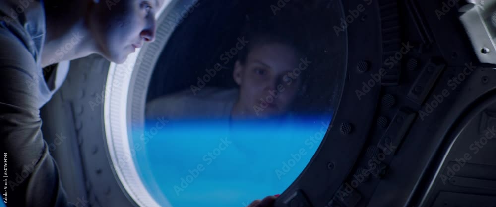 Portrait of Caucasian female astronaut looking through spaceship cupola window. Space exploration, Mars mission. Shot with 2x anamorphic lens