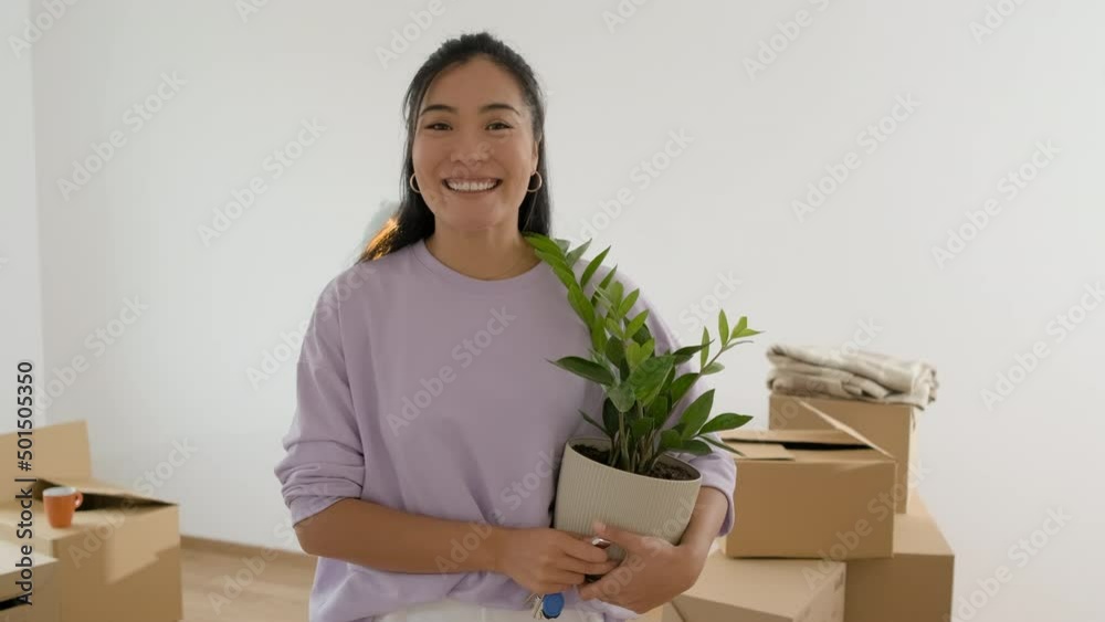 Portrait of young Asian woman in new home holding keys and houseplant in her hands. Portrait of young Asian woman in new home holding keys and houseplant in her hands.