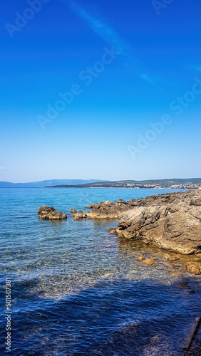 A view on a shallow water in a bay. Sea water is calm and shining with many shades of blue. On the side there are rocks striking out of the sea water. Clear and sunny weather. photo