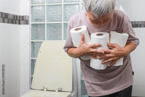 Fototapeta Senior woman carrying holding a lot of toilet paper in bathroom,many rolls of to