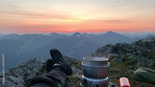 Climber preparing food on Lofoten mountain top in midnight sun sunset glow - pov photo