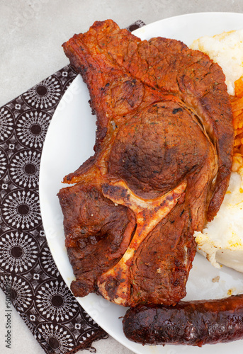  Flat lay of Traditional South African Braai or Shisa nyama, meat cooked on an open flame and traditional side dish of pap and chakalaka. photo