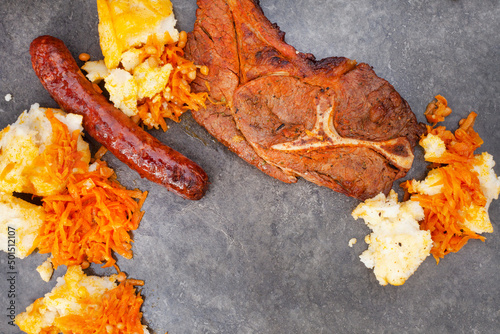  Flat lay of Traditional South African Braai or Shisa nyama, meat cooked on an open flame and traditional side dish of pap and chakalaka. photo