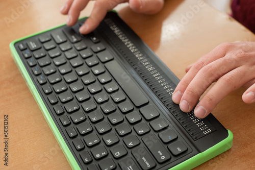A blind man uses a computer with a Braille display and a computer keyboard. Inclusive device. photo