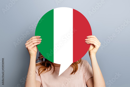 Student girl holds blank white speech bubble with italian flag isolated over grey studio background. woman holding a round information piece of paper dialog photo