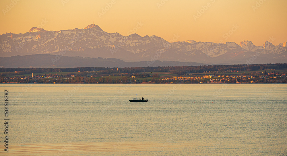 Sonnenaufgang am Bodensee mit Blick auf Wasserfläche, Fischerboot und schweizerisches Ufer mit Alpstein mit dem Gipfel des Säntis und die Churfirsten
