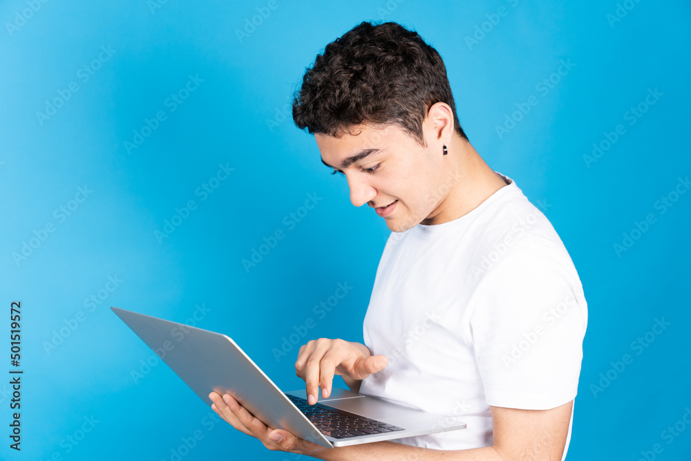 Hispanic young man typing on keyboard of laptop isolated on blue background. Hispanic young man typing on keyboard of laptop isolated on blue background.