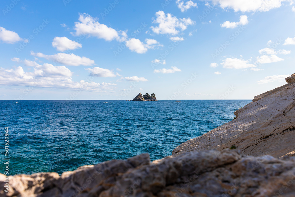 View of  island called Sveta Nedelja (St. Sunday) near Petrovac, Montenegro and blue sky with white fluffy clouds