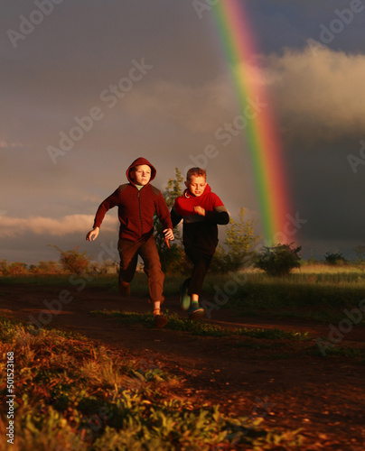 The boys run at sunset against the backdrop of a rainbow.
