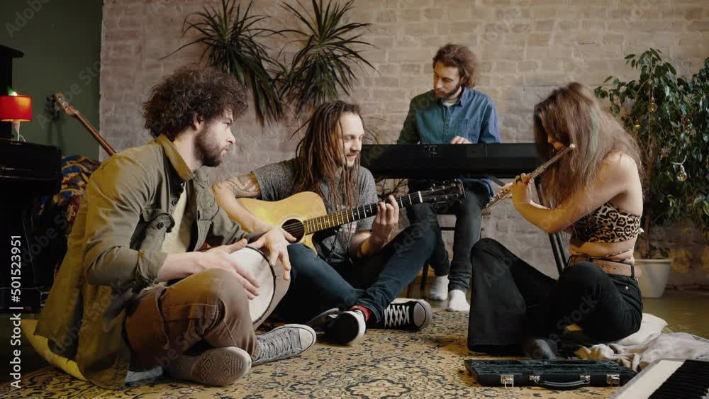 Group of happy friends playing music together at home, sitting together on floor, enjoying sound of rehearsal Group of happy friends playing music together at home, sitting together on floor, enjoying sound of rehearsal